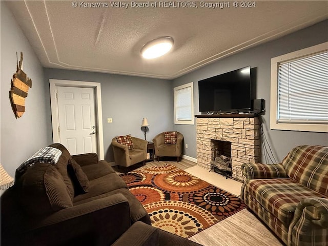 living room featuring a textured ceiling, hardwood / wood-style flooring, and a stone fireplace