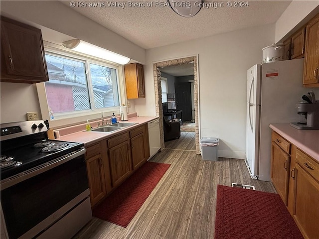 kitchen with a textured ceiling, white appliances, light hardwood / wood-style floors, and sink