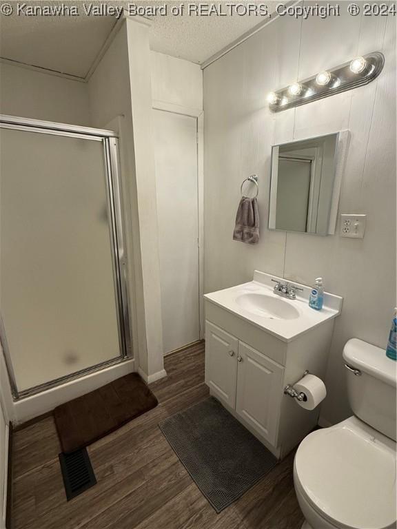 bathroom featuring hardwood / wood-style floors, a textured ceiling, toilet, vanity, and a shower with shower door