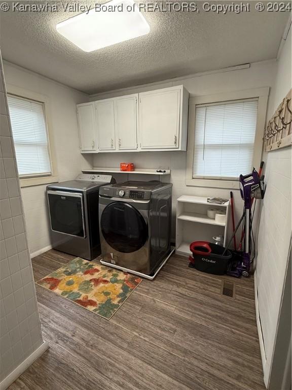 clothes washing area with washer and clothes dryer, cabinets, dark wood-type flooring, and a textured ceiling