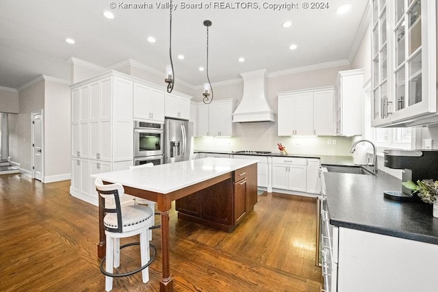 kitchen featuring premium range hood, white cabinets, sink, appliances with stainless steel finishes, and a kitchen island