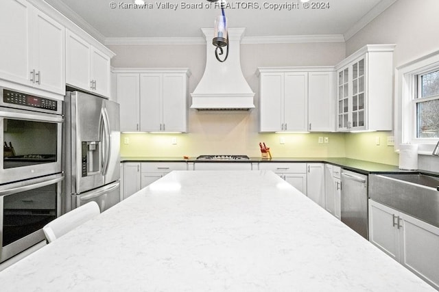 kitchen featuring white cabinetry, premium range hood, decorative light fixtures, appliances with stainless steel finishes, and ornamental molding