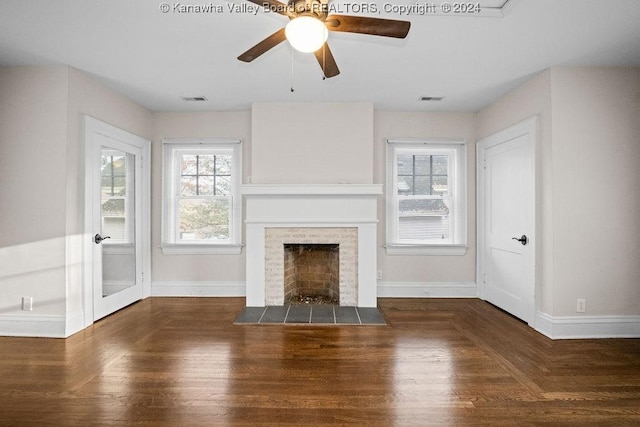 unfurnished living room featuring a tiled fireplace, ceiling fan, plenty of natural light, and dark hardwood / wood-style floors