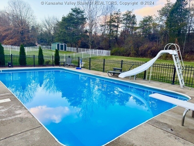 view of swimming pool with a diving board, a storage shed, and a water slide