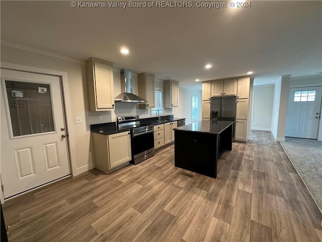 kitchen featuring wall chimney range hood, crown molding, light wood-type flooring, appliances with stainless steel finishes, and a kitchen island