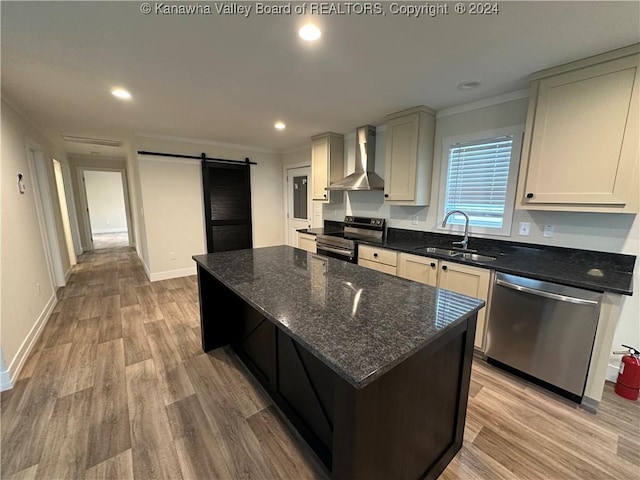 kitchen with sink, wall chimney exhaust hood, a barn door, dark stone countertops, and appliances with stainless steel finishes