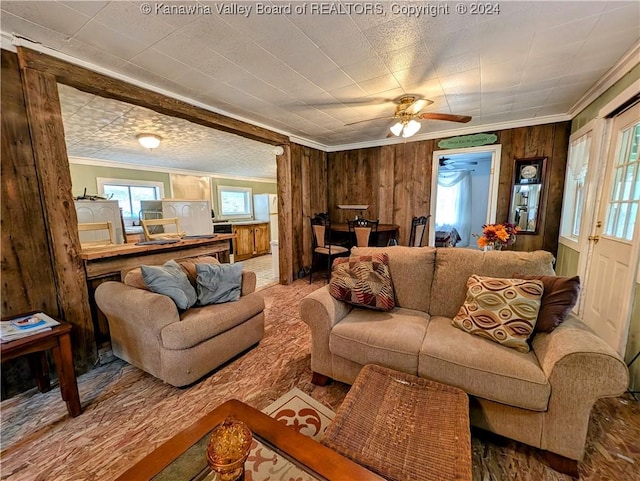 living room with ceiling fan, crown molding, and wood walls