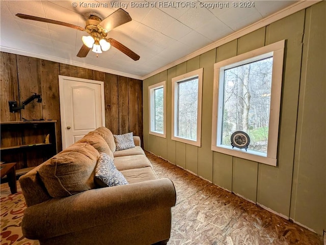 living room featuring ceiling fan, ornamental molding, and wood walls