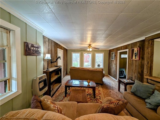 carpeted living room featuring heating unit, ceiling fan, crown molding, and wood walls