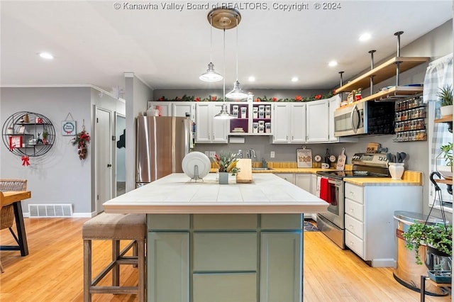 kitchen with appliances with stainless steel finishes, light wood-type flooring, white cabinets, a kitchen island, and hanging light fixtures