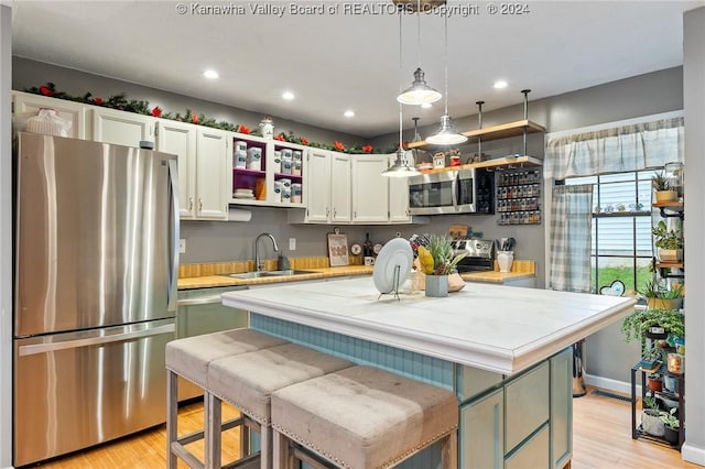 kitchen with light wood-type flooring, stainless steel appliances, sink, a center island, and hanging light fixtures