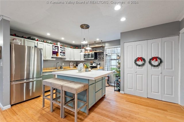 kitchen featuring a kitchen island, light wood-type flooring, decorative light fixtures, and appliances with stainless steel finishes