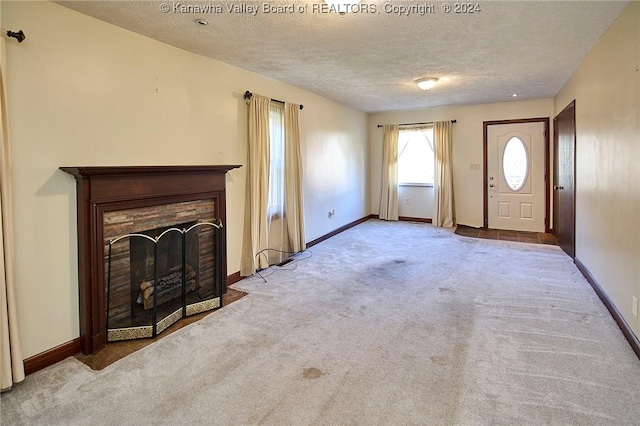 unfurnished living room featuring a textured ceiling, light colored carpet, and a fireplace