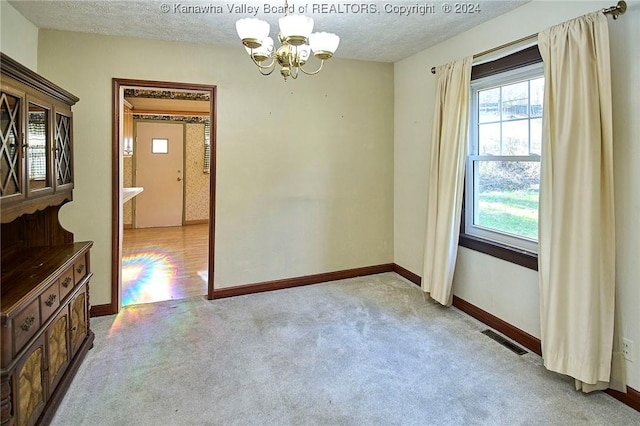 carpeted empty room featuring a textured ceiling and an inviting chandelier