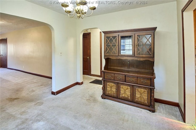 empty room with light carpet, a textured ceiling, and a notable chandelier