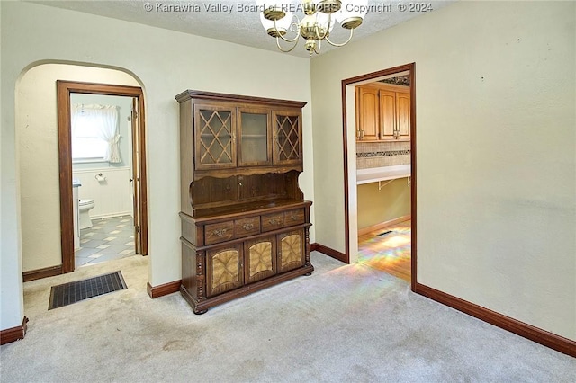 corridor with a notable chandelier, light colored carpet, and a textured ceiling