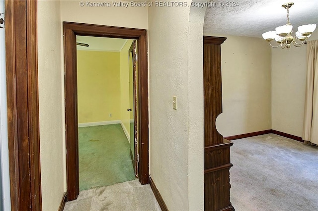 corridor featuring light carpet, a textured ceiling, and an inviting chandelier