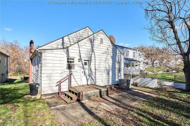 rear view of house featuring central AC unit and a lawn