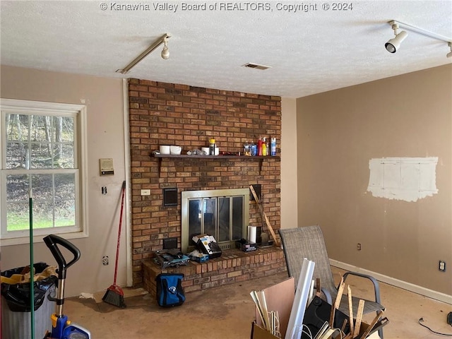 living room with track lighting, a textured ceiling, and a brick fireplace