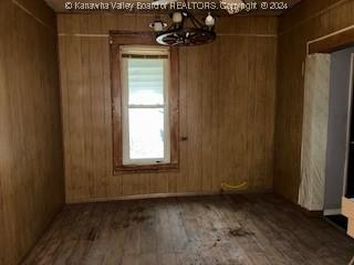 empty room with wood walls, hardwood / wood-style floors, and an inviting chandelier