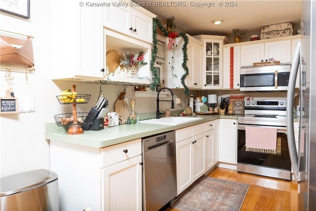 kitchen with appliances with stainless steel finishes, white cabinetry, light hardwood / wood-style flooring, and sink