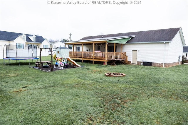 rear view of property featuring a yard, an outdoor fire pit, a trampoline, a playground, and a wooden deck