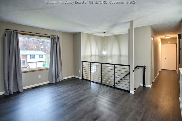 unfurnished room featuring a textured ceiling, dark hardwood / wood-style floors, and an inviting chandelier