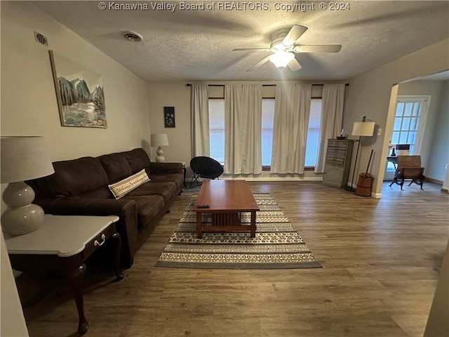 living room with hardwood / wood-style flooring, ceiling fan, and a textured ceiling