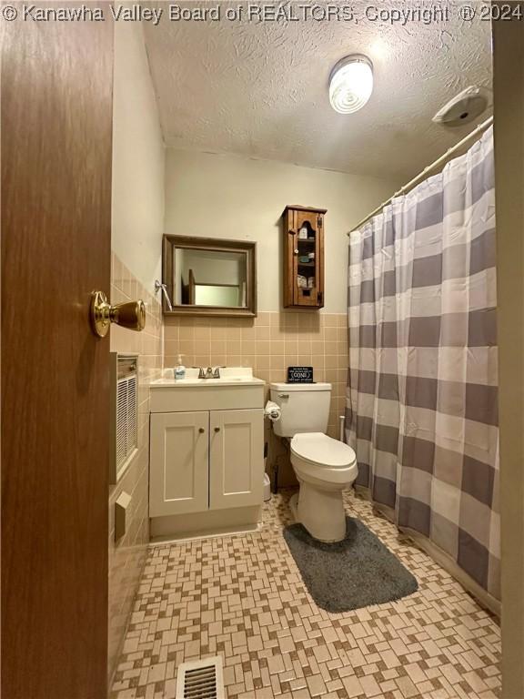 bathroom with a shower with curtain, vanity, a textured ceiling, tile walls, and toilet