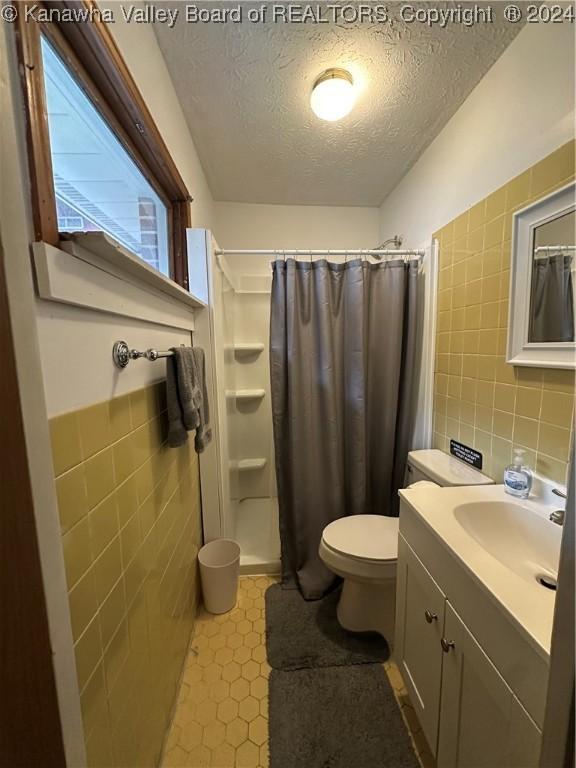 bathroom with a shower with shower curtain, vanity, tile walls, and a textured ceiling