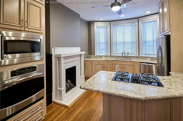 kitchen featuring a tiled fireplace, a peninsula, stainless steel appliances, a ceiling fan, and a sink