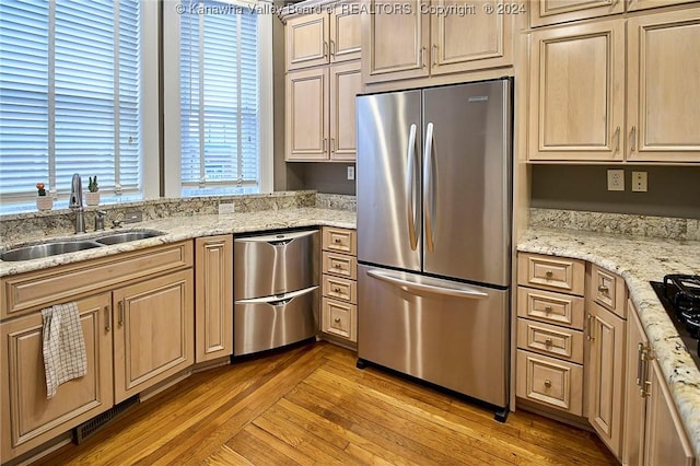 kitchen featuring a sink, light stone countertops, light wood-style floors, and appliances with stainless steel finishes