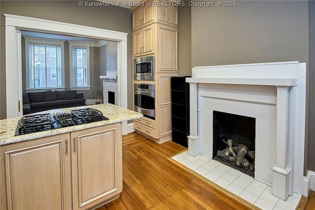 kitchen with light wood finished floors, light brown cabinets, a fireplace with flush hearth, light stone counters, and appliances with stainless steel finishes