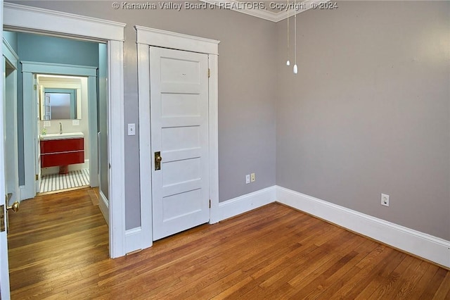 spare room featuring a sink, baseboards, wood finished floors, and crown molding