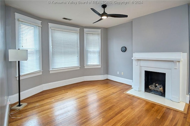 unfurnished living room with visible vents, a fireplace with flush hearth, a ceiling fan, wood-type flooring, and baseboards