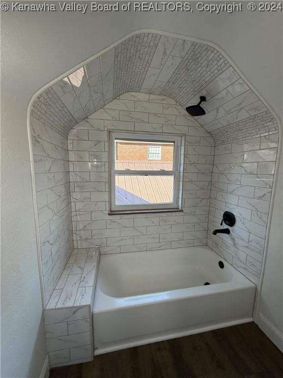 bathroom featuring wood-type flooring, vaulted ceiling, and tiled shower / bath