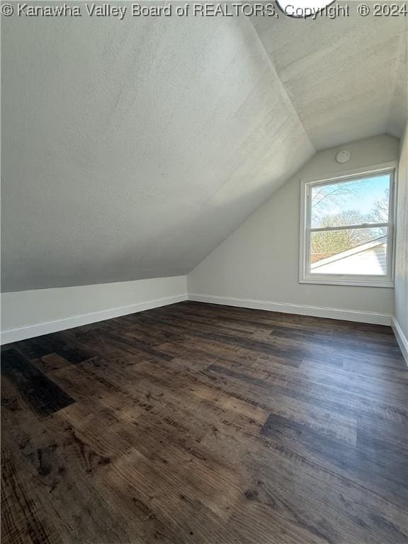 additional living space featuring a textured ceiling, dark wood-type flooring, and vaulted ceiling