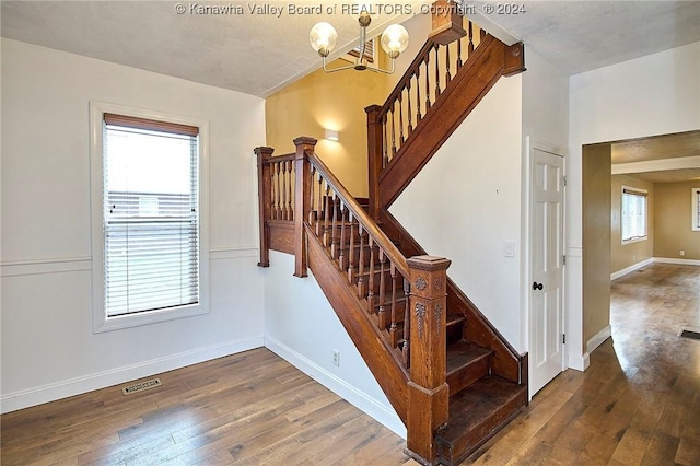 stairs with wood-type flooring and an inviting chandelier