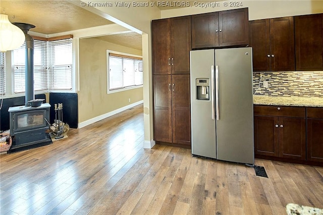 kitchen featuring a wood stove, stainless steel refrigerator with ice dispenser, light hardwood / wood-style flooring, light stone countertops, and tasteful backsplash