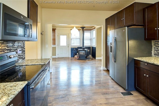 kitchen featuring backsplash, stainless steel appliances, a wood stove, and light stone counters