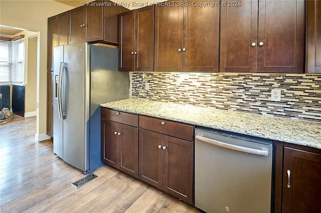 kitchen featuring decorative backsplash, appliances with stainless steel finishes, dark brown cabinets, light hardwood / wood-style floors, and light stone counters