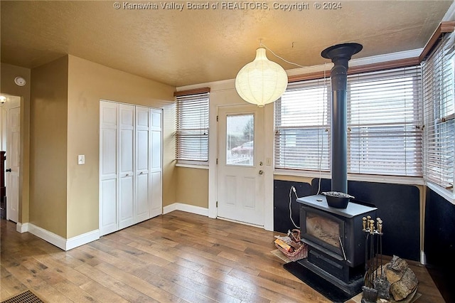 interior space featuring a wood stove, crown molding, light hardwood / wood-style floors, and a textured ceiling