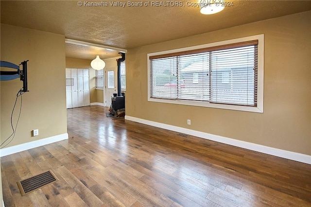 unfurnished living room with hardwood / wood-style flooring, a wood stove, and a textured ceiling