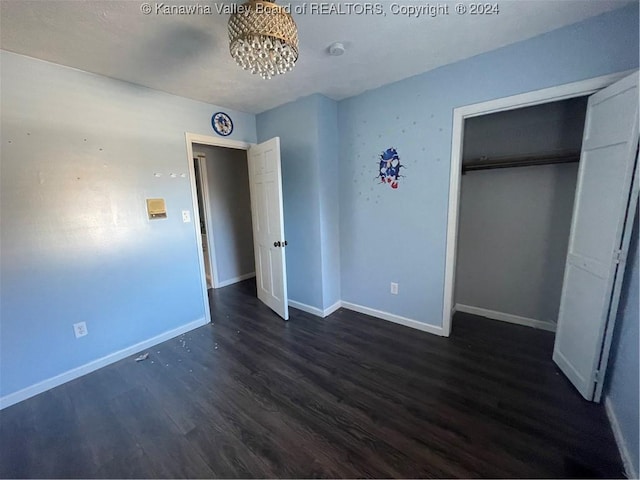 unfurnished bedroom featuring an inviting chandelier, a closet, and dark wood-type flooring