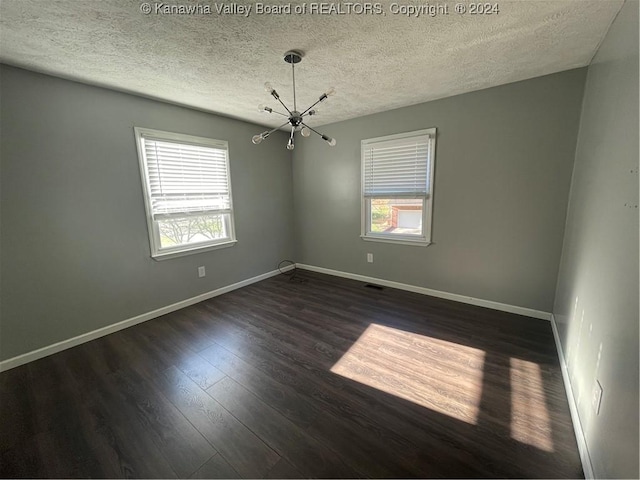 spare room featuring a textured ceiling, dark wood-type flooring, and an inviting chandelier