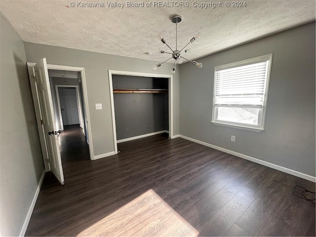 unfurnished bedroom featuring a textured ceiling, a closet, dark wood-type flooring, and a chandelier