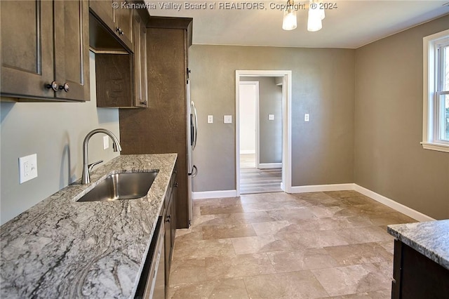 kitchen featuring appliances with stainless steel finishes, light stone counters, dark brown cabinets, sink, and a chandelier