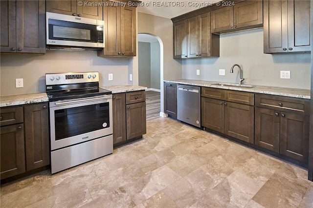 kitchen with dark brown cabinetry, stainless steel appliances, light stone counters, and sink