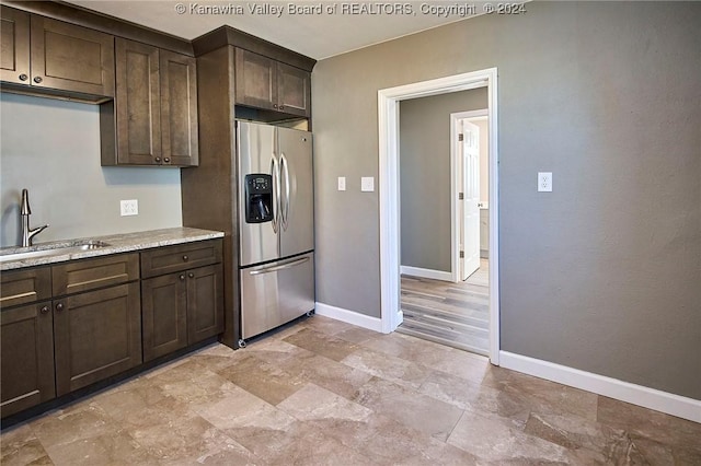 kitchen featuring dark brown cabinets, sink, light stone counters, and stainless steel refrigerator with ice dispenser