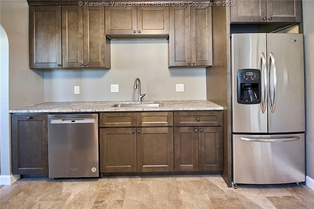 kitchen with light stone countertops, sink, stainless steel appliances, and dark brown cabinets